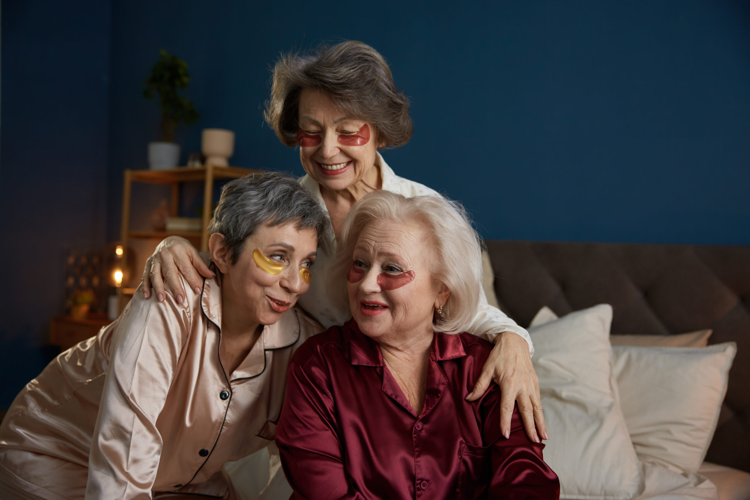 Happy glamour senior female friends wearing nightwear laughing speaking together doing skincare rejuvenation procedure at home. Relaxation and beauty routine on retirement
