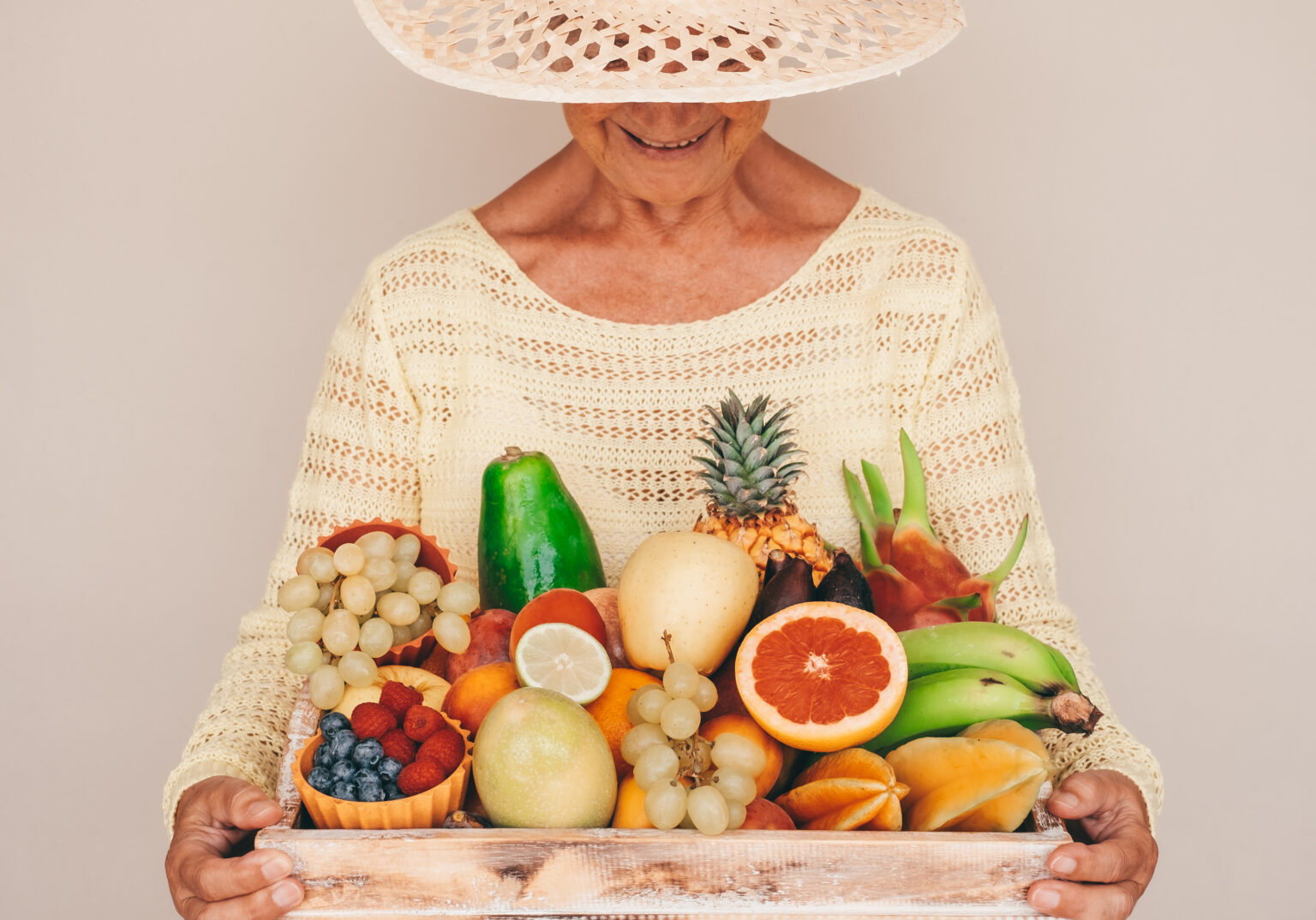 Smiling senior woman in straw hat holding basket full of fresh exotic fruit, healthy lifestyle concept