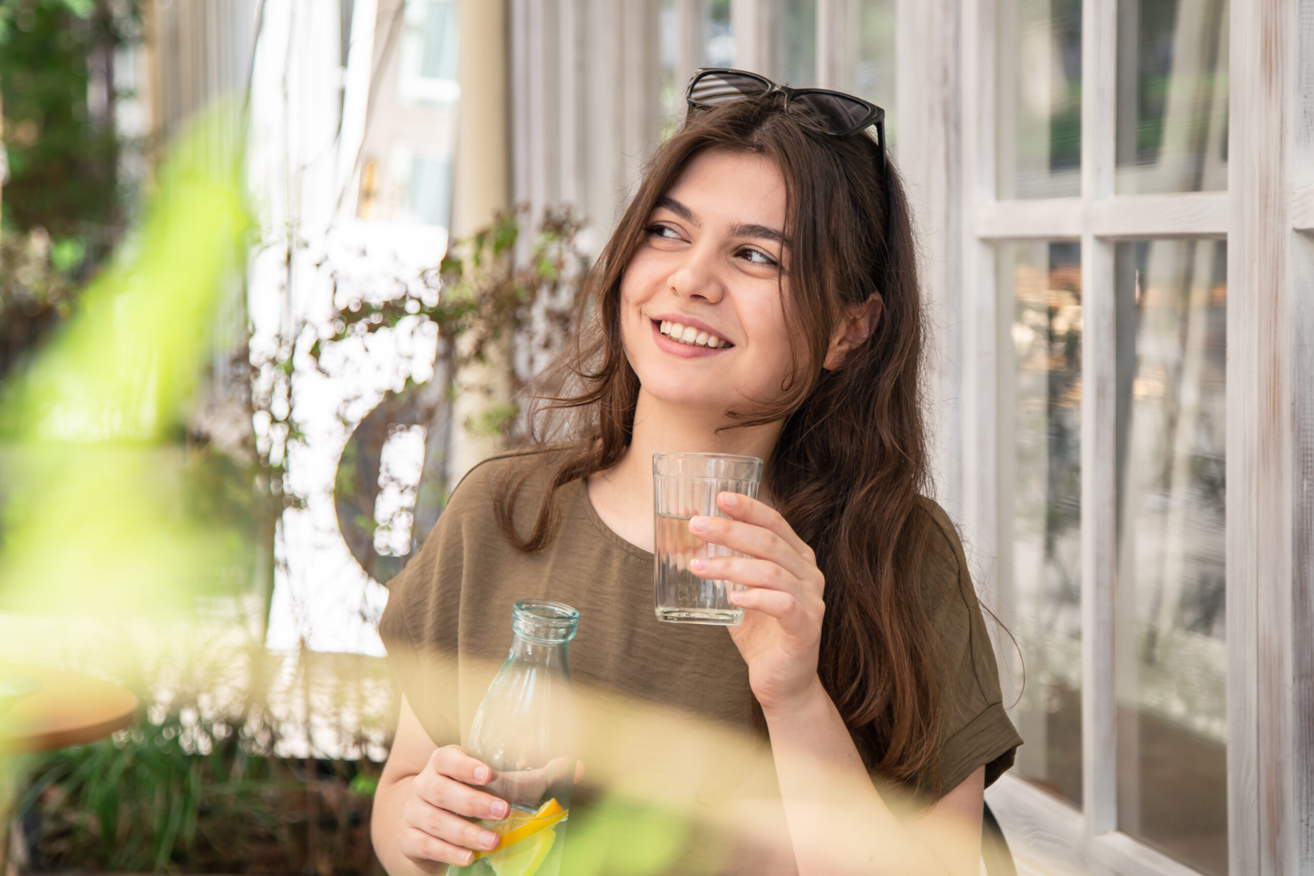 Attractive young woman with a glass of water relaxing outdoors on a hot summer day on the cafe terrace, water balance concept.