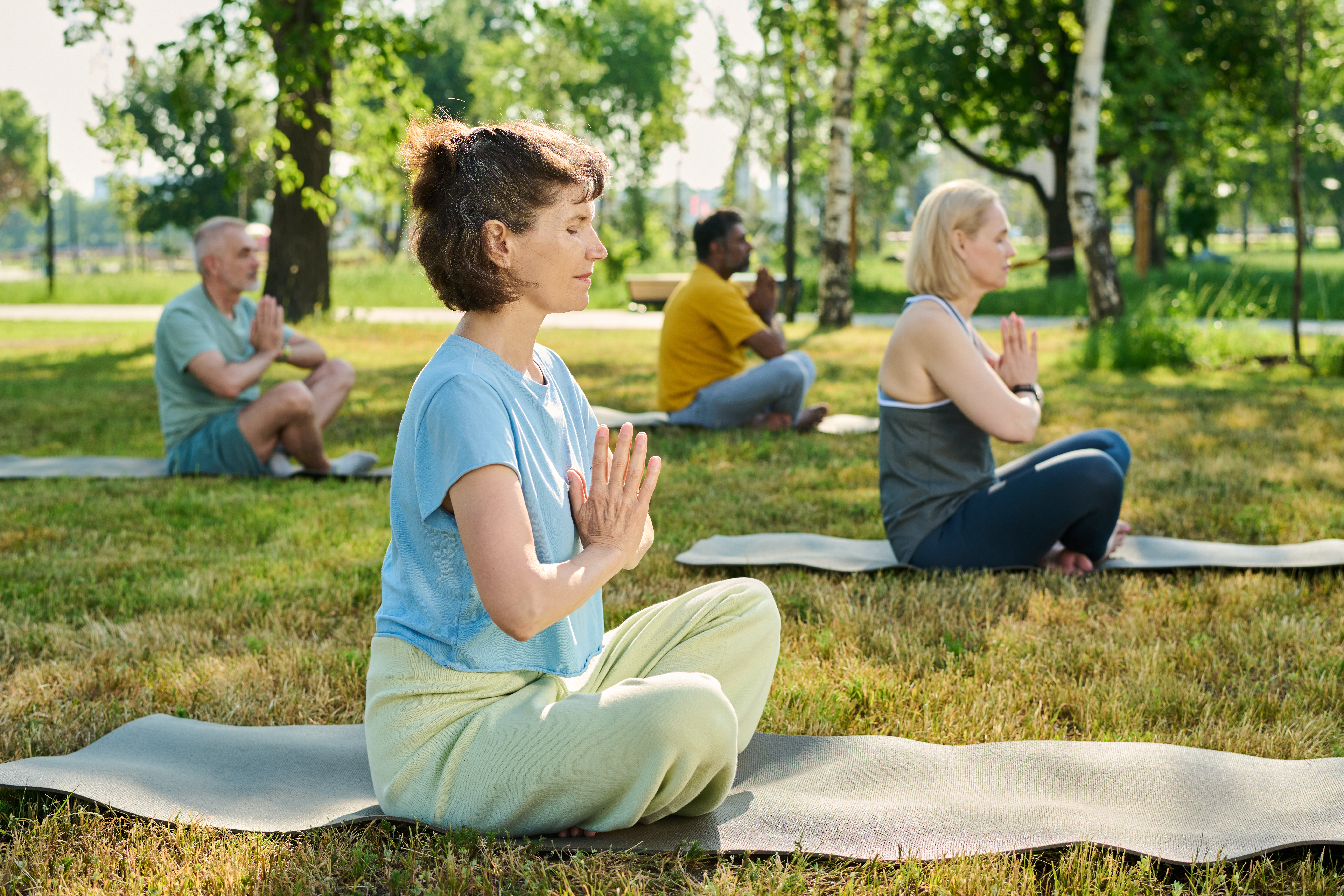 Side view of serene mature woman in t-shirt and sweatpants sitting on mat in natural environment and practicing yoga exercises